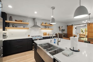 A modern kitchen with a central island, stainless steel appliances, and wooden shelving. - Seasonal Retreat | Private Yard w/Sauna & Spa (Whitefish)