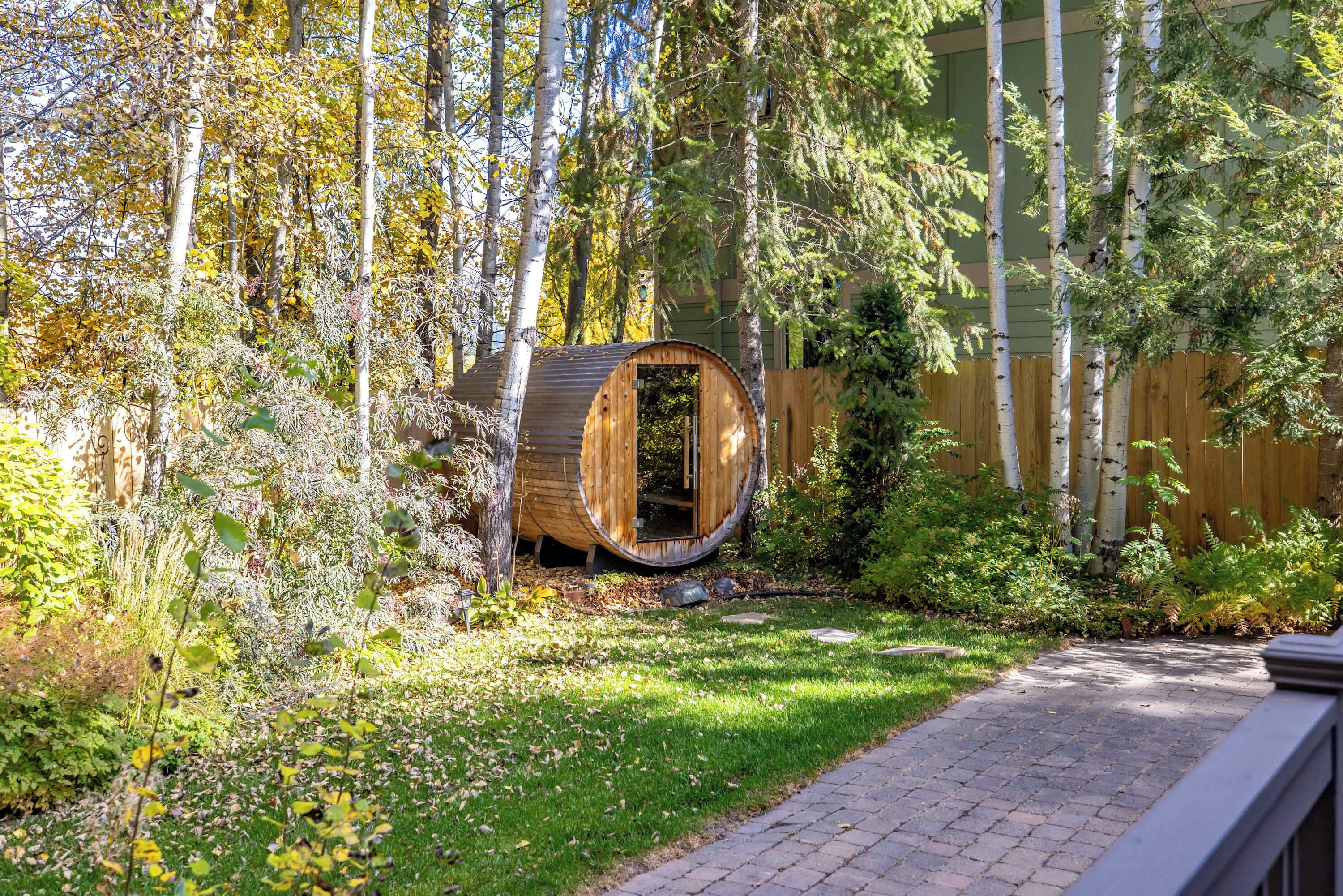 Una estructura de barriles de madera en un jardín, con una valla de madera y árboles al fondo.