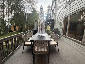 Eine Terrasse mit Esstisch und Stühlen, umgeben von Holzdielen und Blick auf Bäume.