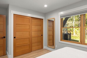 A bedroom with a large wardrobe, a mirror, and a window with a view of trees. - Seasonal Retreat | Private Yard w/Sauna & Spa (Whitefish)