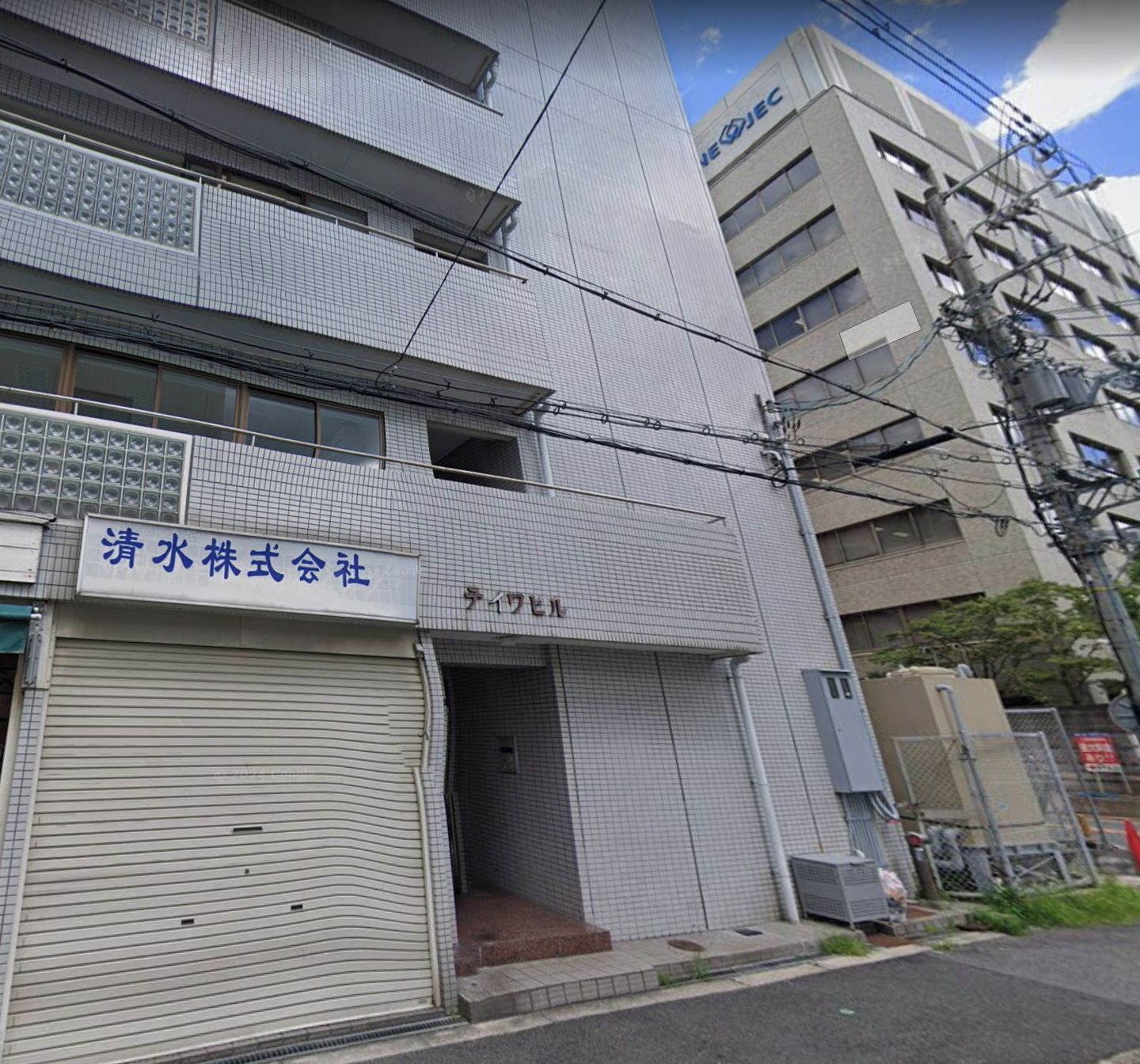 Un bâtiment dont la façade est recouverte de carreaux et sur lequel on peut lire l'inscription « Shimizu Kabushiki Gaisha ».