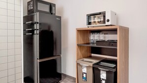 Un angolo cottura con un frigorifero nero, un forno a microonde e un tostapane su un ripiano in legno.