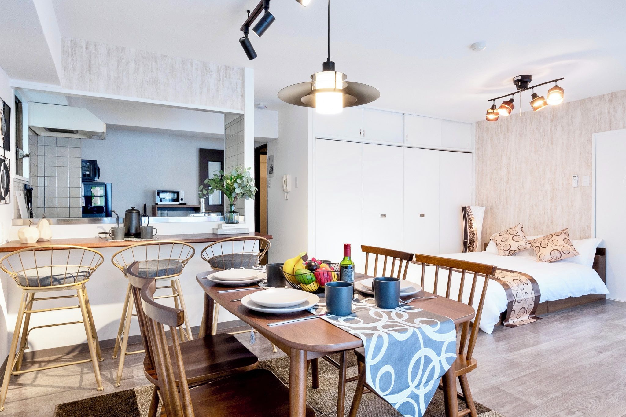 Une cuisine moderne avec des meubles blancs, un coin repas avec une table et des chaises en bois, et un salon avec un canapé et un plaid à motifs.
