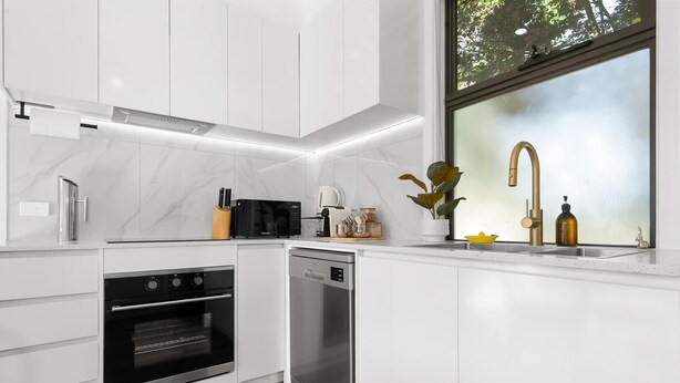 Een moderne keuken met witte kastjes, roestvrijstalen apparatuur en een raam met uitzicht op bomen.