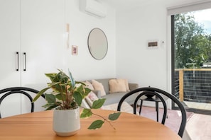 A modern interior with a wooden dining table, a potted plant, a sofa, and a large mirror on the wall. - Brand-New Fernview 2BR w/ 2 Ensuites | Foothills (Ferntree Gully)