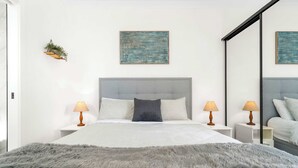 Een moderne slaapkamer met een groot bed, twee bedlampen, een zachte grijze plaid en twee abstracte schilderijen aan de wand.