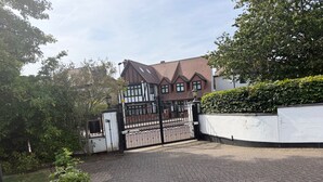 A gated residential area with a paved driveway, a white wall, and a hedge.
