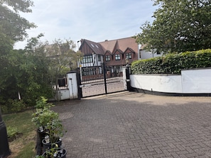 A gated residential area with a paved driveway, a white wall, and a hedge.