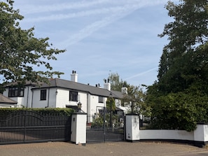A white building with a gated entrance, surrounded by greenery.