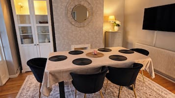 A dining area with a table, chairs, a cabinet, a mirror, a lamp, and a television on the wall.