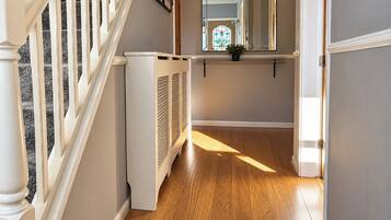 A hallway with a wooden floor, white walls, and a staircase with white railings.