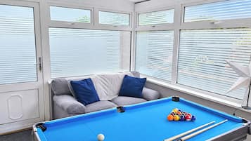 A pool table with balls, a sofa with blue cushions, and a window with blinds.