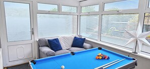 A pool table with balls, a sofa with blue cushions, and a window with blinds.
