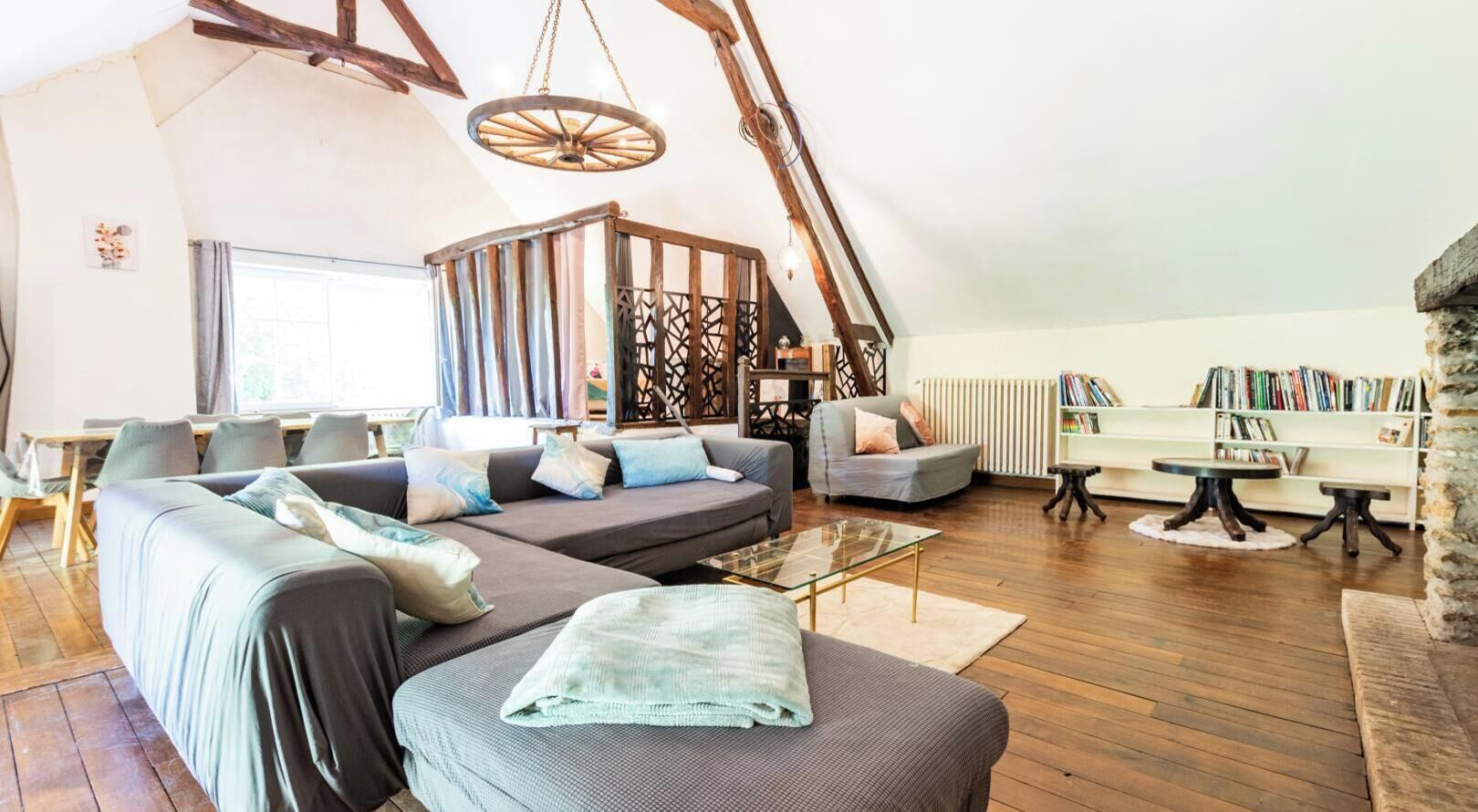 A cozy loft-style living room with a sectional sofa, a glass coffee table, and a wooden ceiling.