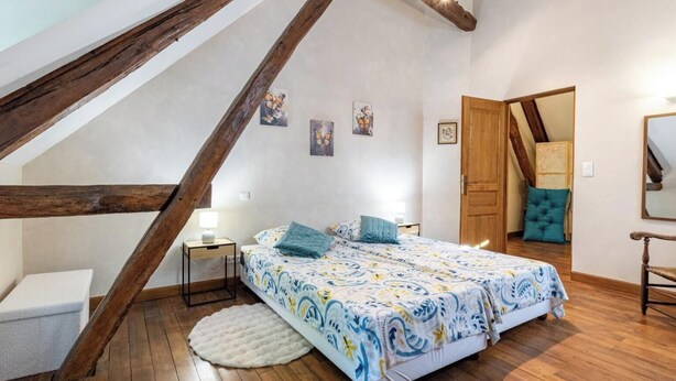 Quarto com teto inclinado, cama com roupa de cama estampada, mesa de cabeceira com abajur e tapete redondo.