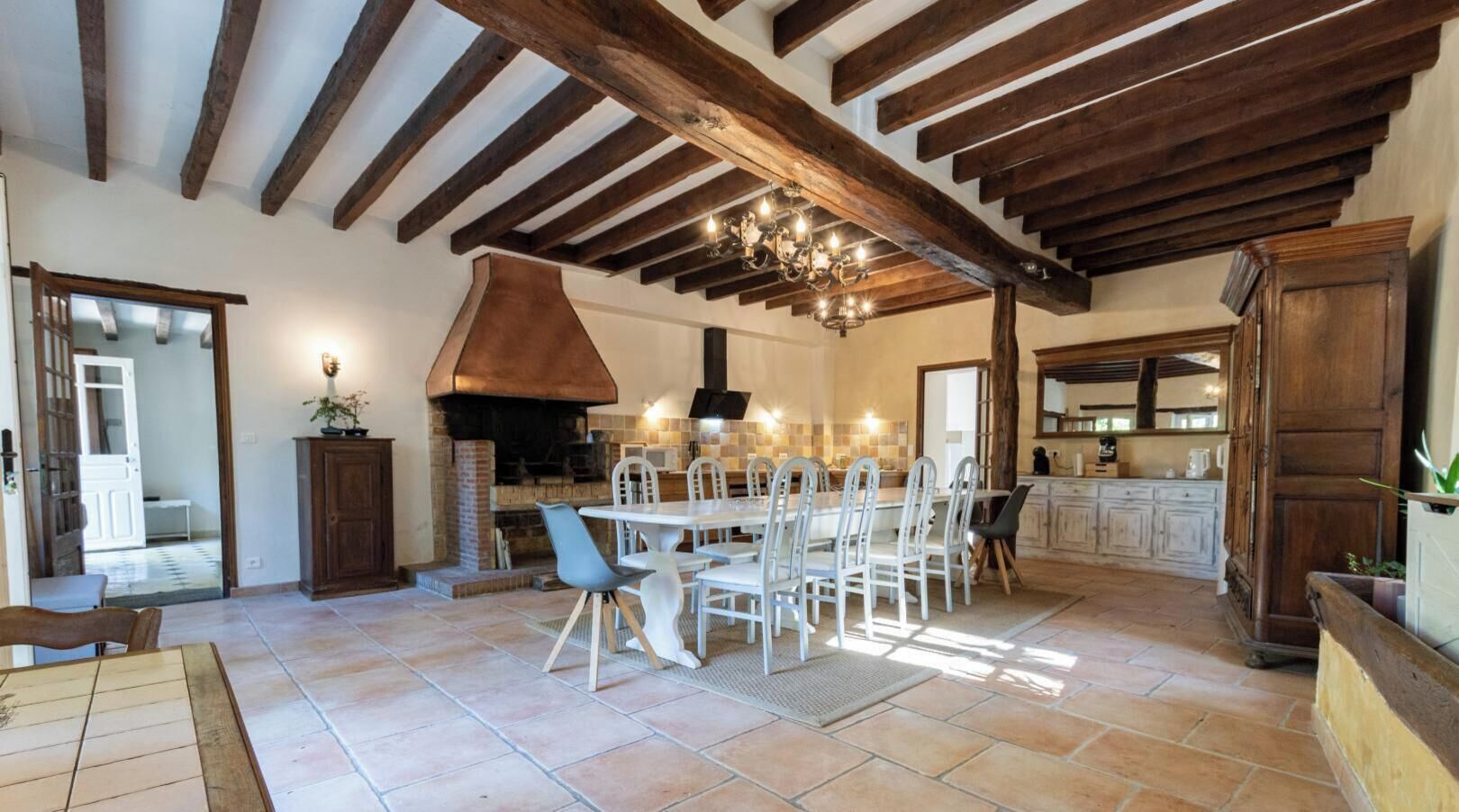 A spacious kitchen with a large dining table, wooden beams, and a brick oven.