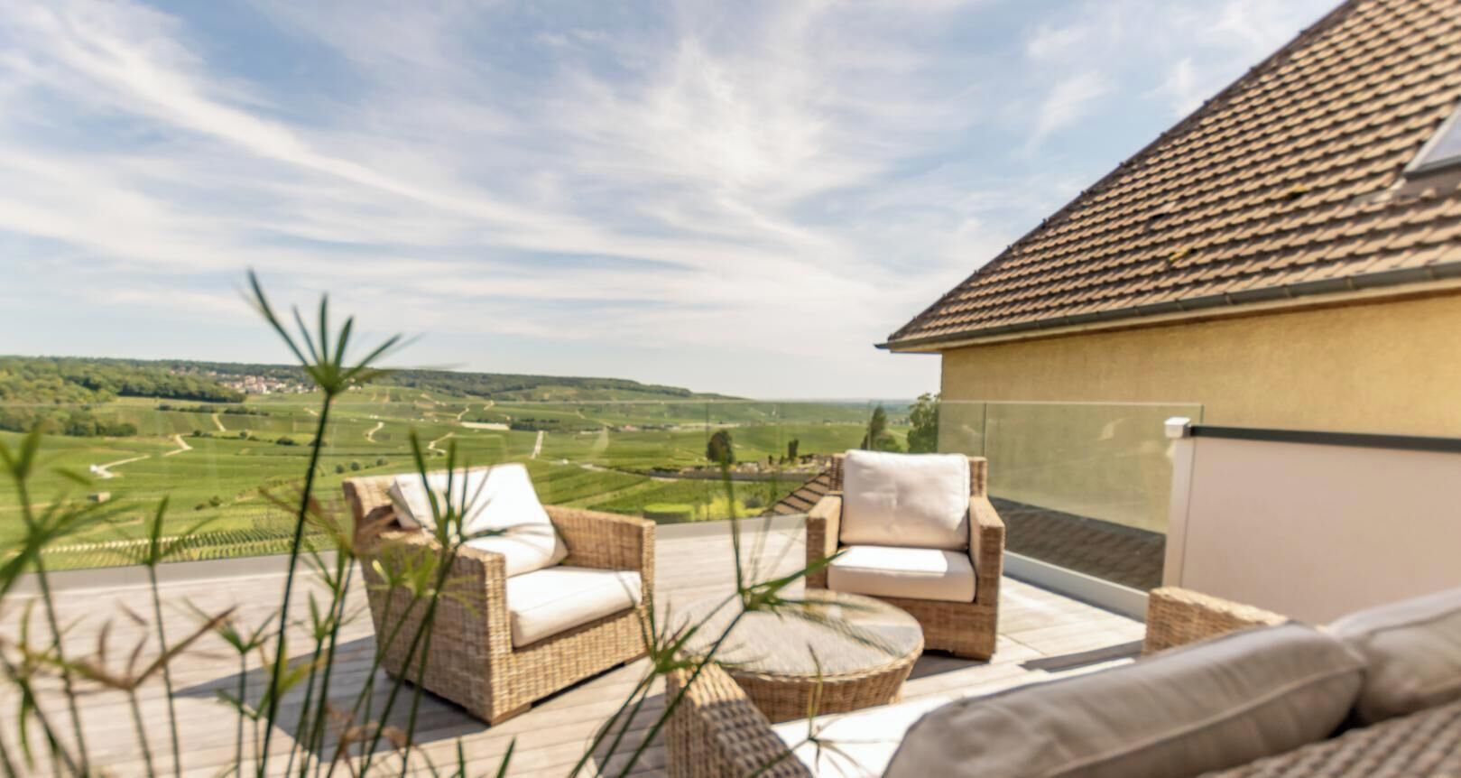 A balcony with wicker furniture and a view of a green landscape.