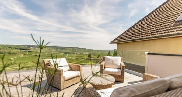 A balcony with wicker furniture and a view of a green landscape.