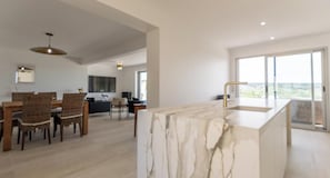 A modern kitchen with a marble countertop and a view of the outdoors through large windows.
