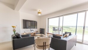 Una sala de estar moderna con un televisor grande, asientos cómodos y vistas amplias a través de ventanas grandes.