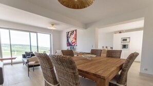 Un comedor amplio con una gran mesa de madera y sillas de mimbre, una cocina moderna con armarios blancos y un amplio ventanal con vistas al exterior.