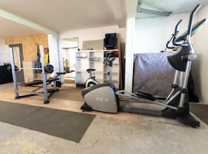 A home gym with a stationary bike, elliptical, and weight bench.