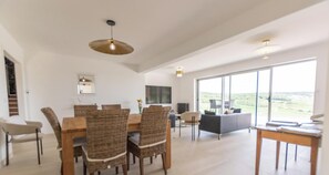 A spacious living area with a dining table and chairs, a sofa, and a large window offering a view.