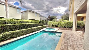 A swimming pool with a hot tub, surrounded by hedges and a brick patio. - Spacious 8BR Disney-Area Home| Pool & Home Theater (Kissimmee)