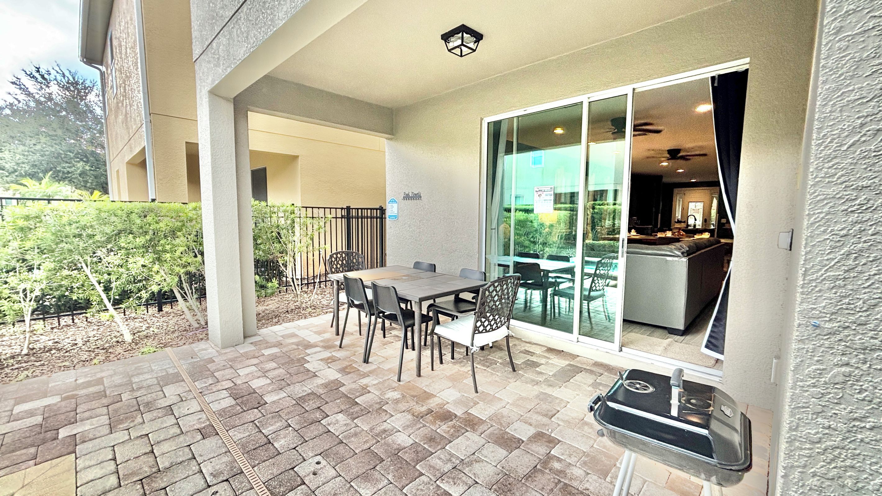 An outdoor patio with a table and chairs, a grill, and a view into the building.