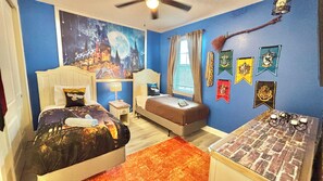 Une chambre avec deux lits, une table de chevet, une fenêtre avec des rideaux et un mur décoré de différentes banderoles.