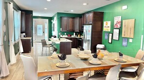 Une cuisine moderne avec des meubles de couleur bois foncé, un réfrigérateur en acier inoxydable et un coin repas doté d’une table en verre pour quatre personnes.