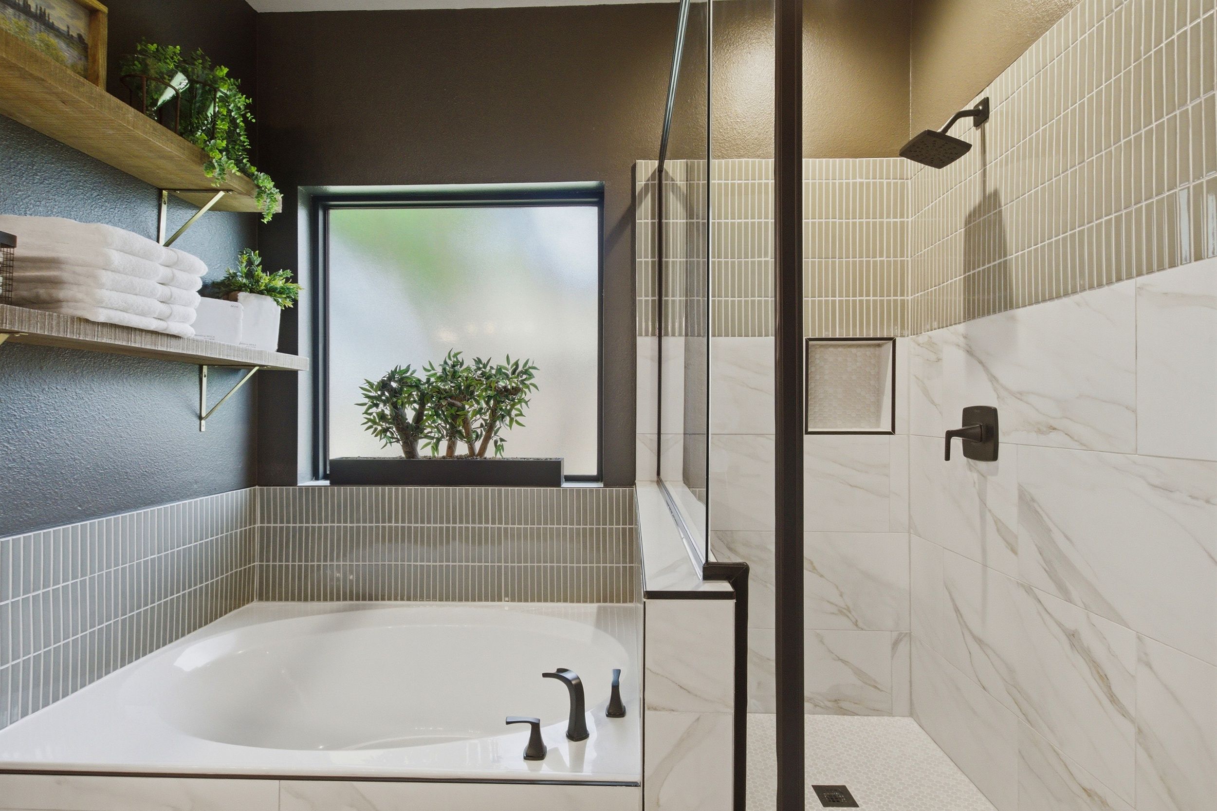 Un baño moderno con una bañera independiente, ducha con cerramiento de vidrio y ventana con vistas a zonas verdes.