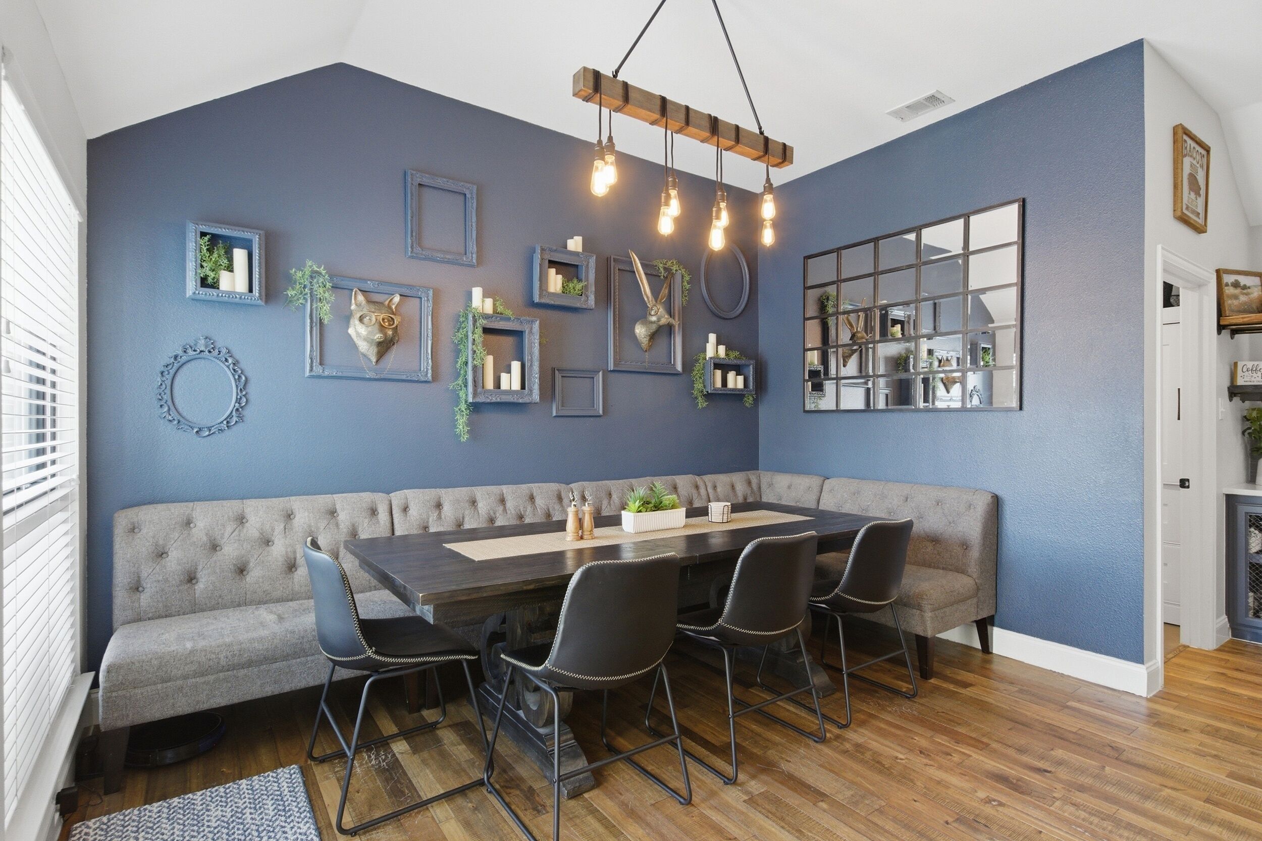 Un comedor con pared azul oscuro, una mesa de madera y un banco tapizado en gris.