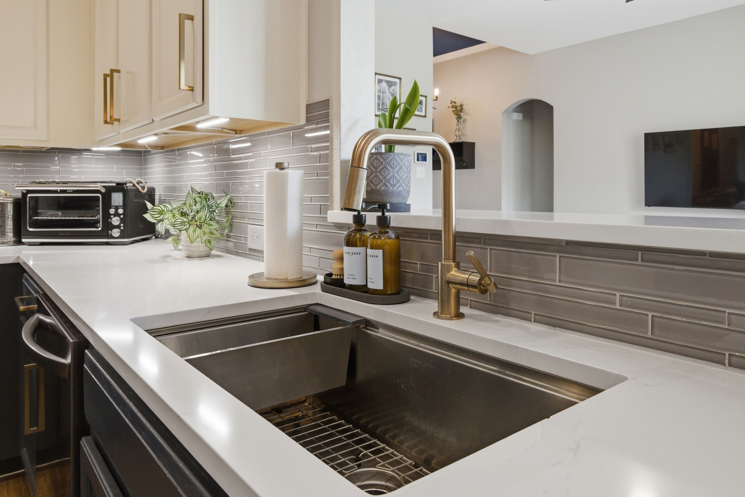 A modern kitchen with a stainless steel sink, a built-in oven, and a countertop with a toaster and a potted plant.