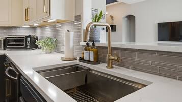 A modern kitchen with a stainless steel sink, a built-in oven, and a countertop with a toaster and a potted plant.