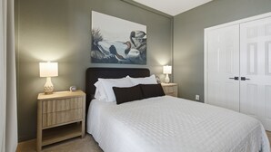 Un dormitorio con una cama, dos mesitas de noche, una lámpara de noche, un cuadro en la pared y una puerta blanca.