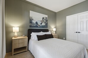 A bedroom with a bed, two bedside tables, a nightstand, a wall-mounted painting, and a white door. - Family Getaway Near Grandscape & Universal Kids (The Colony)