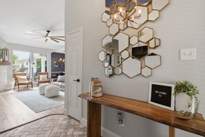 A modern interior with a hexagonal mirror wall, a welcome sign, and a wooden console table. - Family Getaway Near Grandscape & Universal Kids (The Colony)