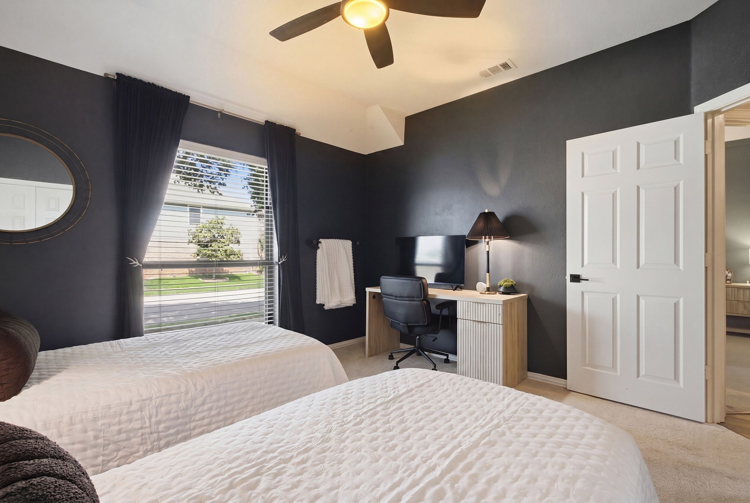 A bedroom with two beds, a desk, a chair, a TV, and a ceiling fan.