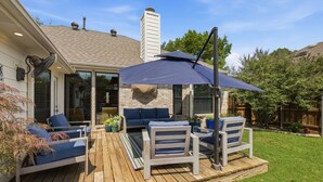 Una terraza con mobiliario exterior, un área cubierta con una sombrilla y una chimenea de ladrillo.