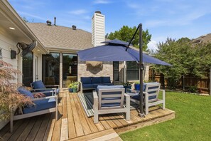 A deck with outdoor furniture, a covered area with an umbrella, and a brick fireplace. - Family Getaway Near Grandscape & Universal Kids (The Colony)