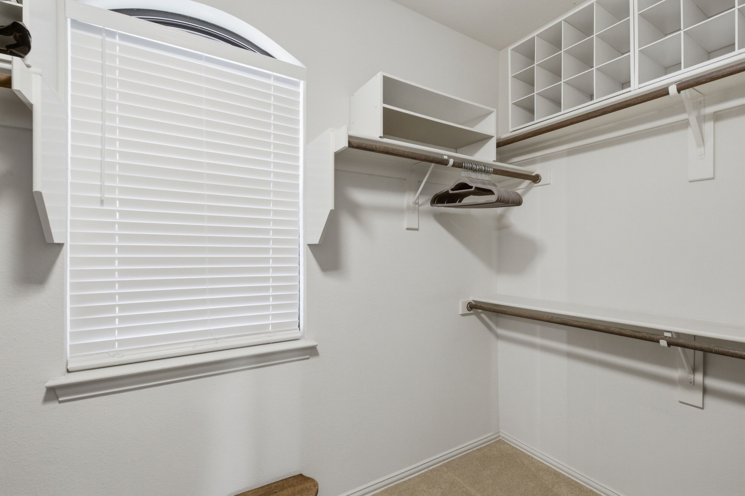 A closet with built-in shelves, a hanging rod, and a window with blinds.