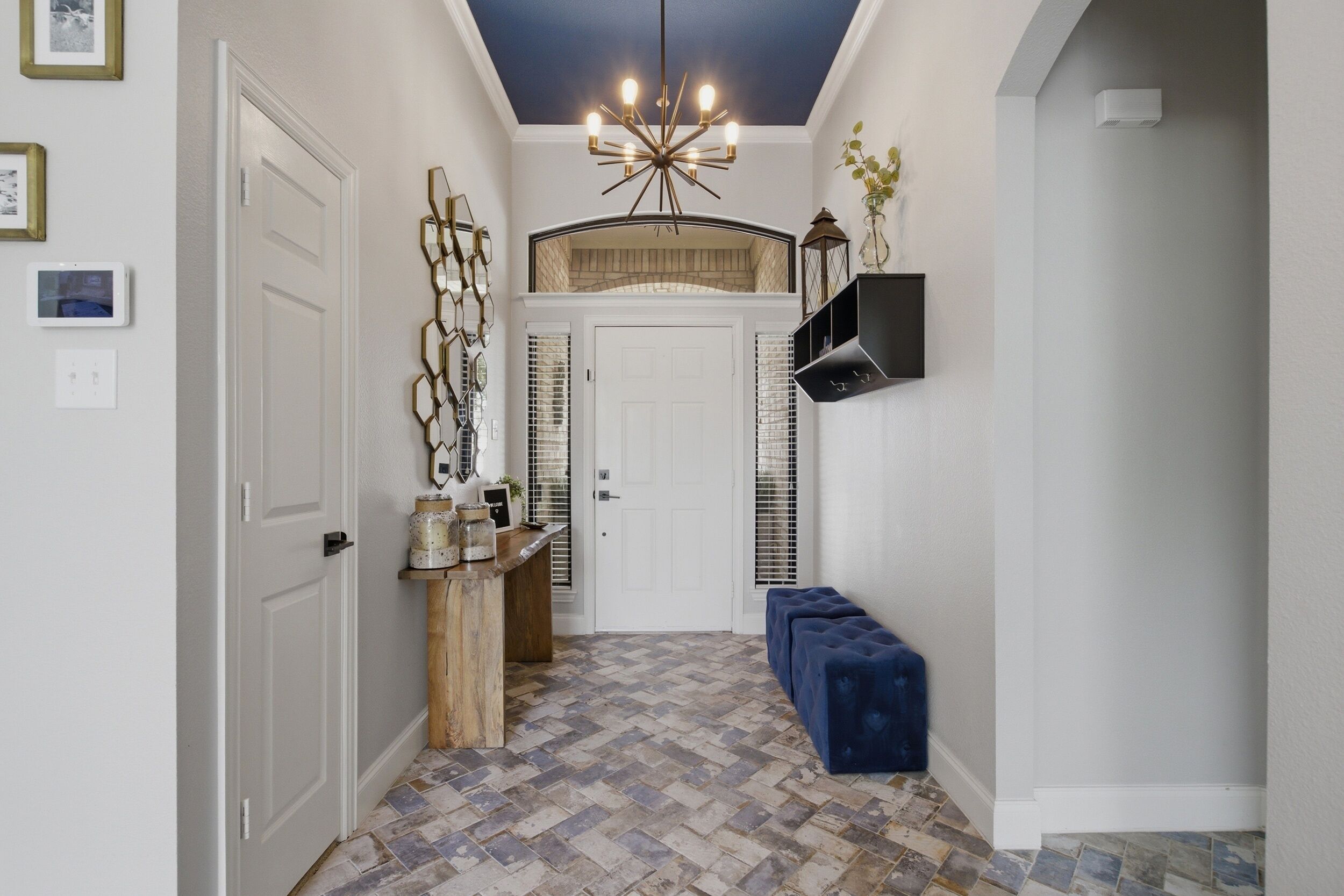 A hallway with a patterned floor, a chandelier, a bench, and a door leading to another room.