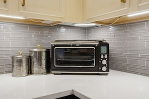 A kitchen with a built-in toaster oven, two stainless steel containers, and a white countertop. - Family Getaway Near Grandscape & Universal Kids (The Colony)
