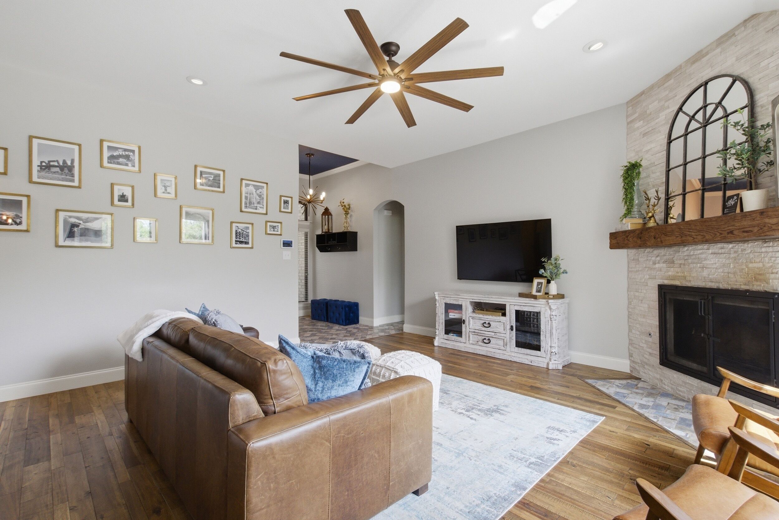 A living room with a brown leather sofa, a flat-screen TV mounted on the wall, and a fireplace with a mantel.