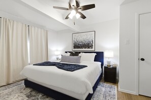Ein Hotelzimmer mit einem Bett, einem Deckenventilator, einem Gemälde, zwei Nachttischlampen und einer Tür.
