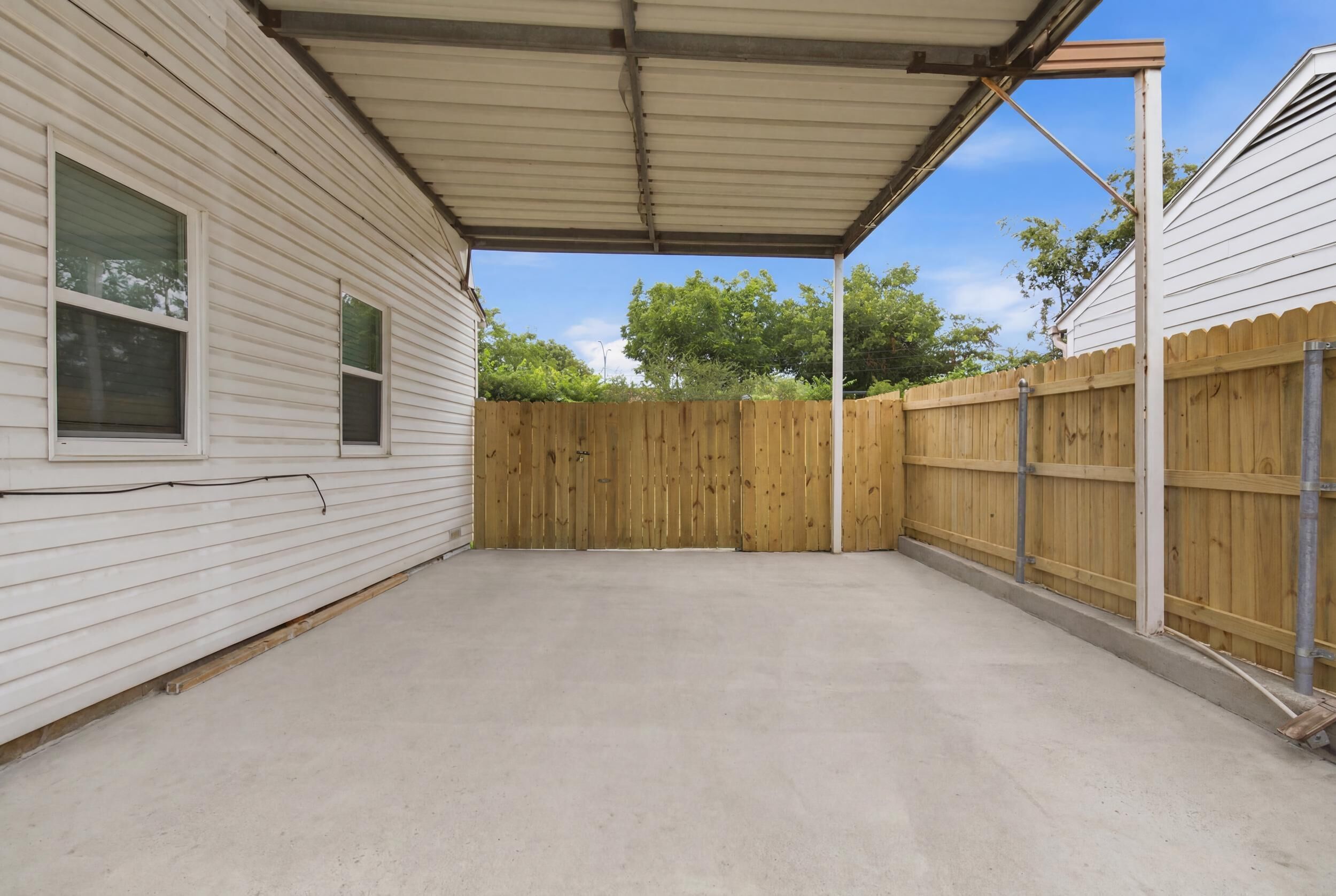 Un patio cubierto con suelo de concreto, cerca de madera y una casa con revestimiento.