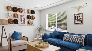 Una sala de estar moderna con un sofá azul, una mesa de centro y una colección de sombreros en estanterías.