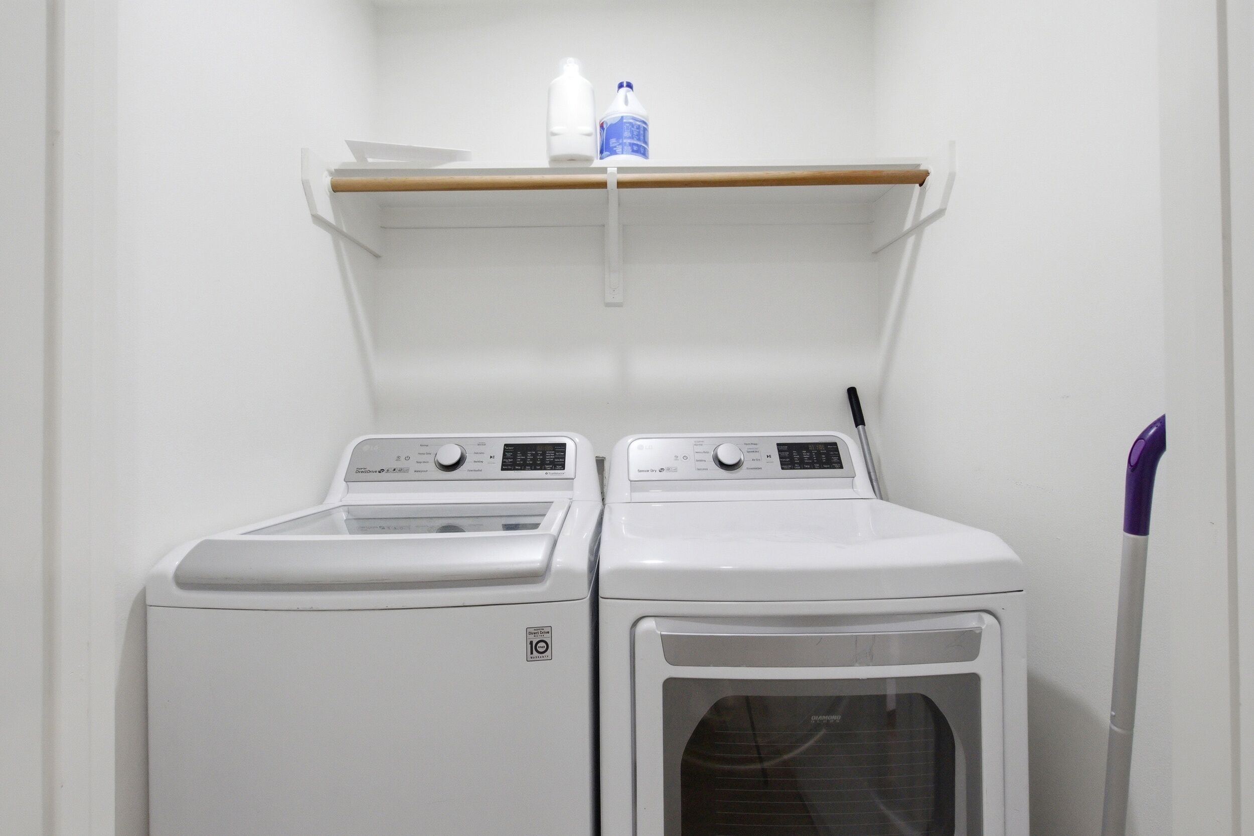 A laundry area with two white washing machines and a shelf above them.