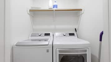A laundry area with two white washing machines and a shelf above them.